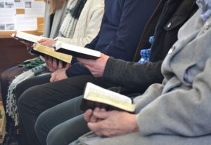 A row of people sitting holding open Bibles