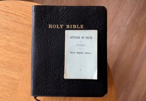 A black Bible on a table with a booklet on top