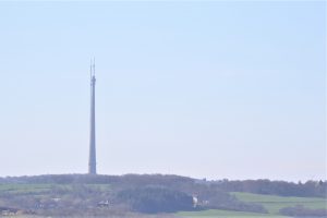 A landscape photo with green fields and Emley Moor Mast against a blue sky