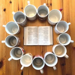 A circle of mugs with an open Bible in the middle